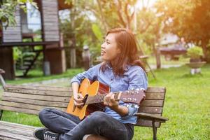 bella giovane donna che suona la chitarra seduta su una panchina, concetto di tempo felice. foto