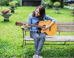 bella giovane donna che suona la chitarra seduta su una panchina, concetto di tempo felice. foto