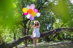 giovane ragazza adolescente seduta su un albero e con palloncini in mano foto