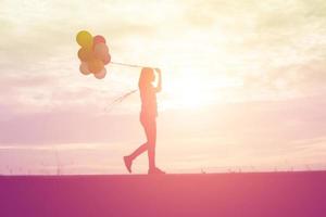 silhouette di giovane donna che tiene colorato di palloncini con il tramonto foto