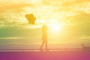 silhouette di giovane donna che tiene colorato di palloncini con il tramonto foto