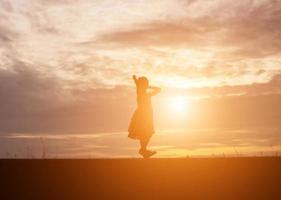 una silhouette di una bambina felice le braccia della sua amorevole madre per un abbraccio, davanti al tramonto nel cielo in una giornata estiva. foto