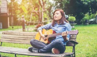 bella giovane donna che suona la chitarra seduta su una panchina, concetto di tempo felice. foto