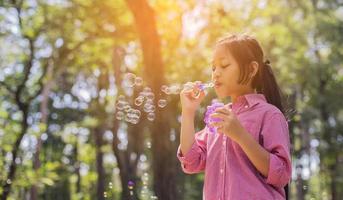 bambina carina che indossa una camicia rosa che soffia bolle nel parco, stile vintage. foto