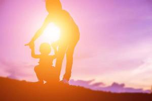 una silhouette di una bambina felice le braccia della sua amorevole madre per un abbraccio, davanti al tramonto nel cielo in una giornata estiva. foto