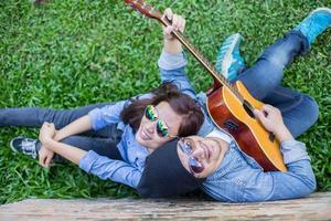 uomo hipster che suona la chitarra per la sua ragazza all'aperto contro un muro di mattoni, godendo insieme. foto