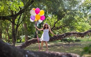 giovane ragazza adolescente seduta su un albero e con palloncini in mano foto