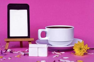 lavagna con tazza di caffè bianca, blocco di legno e fiori su sfondo rosa. foto