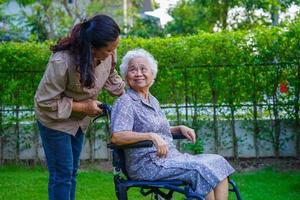 il caregiver aiuta il paziente con disabilità della donna anziana asiatica seduto su una sedia a rotelle nel parco, concetto medico. foto