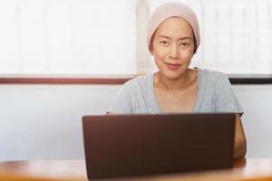 donna che indossa un cappello di lana che lavora al computer portatile e guarda la fotocamera a casa. foto