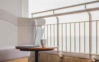 laptop aperto con tazza di caffè sul tavolo di legno sul balcone con vista sull'oceano. foto