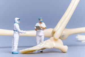 medico di persone in miniatura con un osso umano gigante su sfondo grigio foto