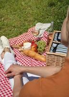 giovane donna irriconoscibile in pantaloni bianchi fuori che fa picnic, mangia e suona la chitarra, vista da dietro foto