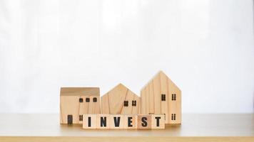 concetto di investimento immobiliare. blocco di legno con testo investire e case modello, crescita immobiliare in futuro, finanza, banche, prestiti e trading. foto