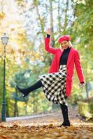 donna contenta in abbigliamento elegante che alza la gamba nel parco autunnale foto