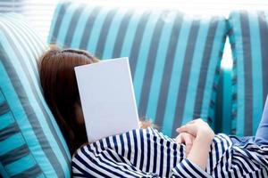 bella giovane donna asiatica che dorme sul divano con il libro che copre il viso perché legge il libro con la preparazione dell'esame di college, ragazza assonnata con stanco in modo che il concetto di svago, relax e istruzione. foto