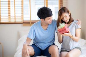 bella giovane coppia asiatica innamorata confezione regalo a sorpresa in camera da letto a casa, anniversario di famiglia con gioia e romanticismo insieme moglie e marito con relazione, celebrando il concetto di San Valentino. foto