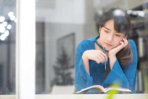 bella giovane scrittrice asiatica sorridente pensando idea e scrivendo su taccuino o diario con felice, lo stile di vita della ragazza asiatica è studente, lavoro di pianificazione femminile, istruzione e concetto di business. foto