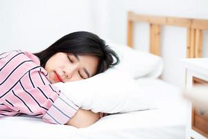 ritratto di bella giovane donna asiatica dormire sdraiato a letto con la testa sul cuscino comodo e felice con il tempo libero, ragazza con relax per il concetto di salute e stile di vita. foto