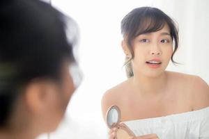 ritratto bella giovane donna asiatica che applica soffio di cipria sulla guancia trucco di specchio cosmetico, bellezza della ragazza con la pelle viso sorriso in camera da letto, concetto di salute e benessere. foto