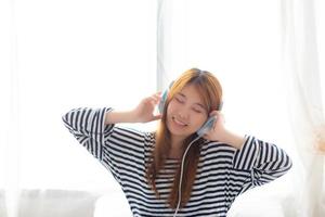 la bella giovane donna asiatica si diverte e si diverte ad ascoltare musica con la cuffia seduta in camera da letto, la ragazza si rilassa con il concetto di auricolare, tempo libero e tecnologia. foto