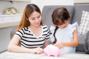 madre e figlia asiatiche che mettono la moneta nel salvadanaio, mamma e bambino con la famiglia del conto di deposito risparmiano insieme soldi per il futuro, concetto di conto finanziario. foto