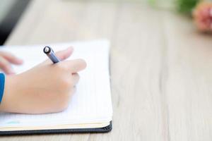 primo piano mano donna asiatica seduta studio e apprendimento scrivere taccuino e diario sul tavolo al negozio di caffè, compiti ragazza, donna scrittrice d'affari che lavora sul tavolo, concetto di istruzione. foto