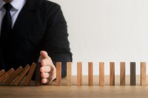 gestione del rischio, la mano dell'uomo d'affari ferma la continua caduta di domino di legno, ferma l'impatto della crisi aziendale. copertura per risolvere i problemi aziendali per il successo. foto