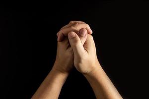 la mano dell'uomo che gli tiene la mano in preghiera ha uno sfondo nero. foto