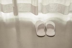 pantofole bianche da tende trasparenti bianche e luce solare morbida, concetto di vacanza foto