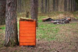 cestino della spazzatura in legno arancione brillante nel punto di riposo della foresta tra i tronchi d'albero sull'erba verde in primavera foto