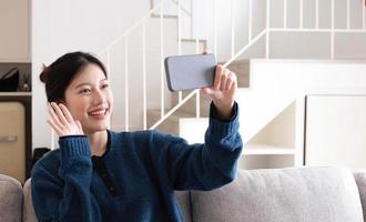ritratto bella giovane donna asiatica usa il telefono cellulare intelligente sul divano nell'interno del soggiorno foto
