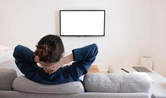 dietro di una giovane donna asiatica che guarda la tv a schermo bianco sul divano di casa foto