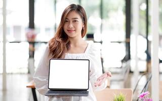 felice giovane donna asiatica vestiti su sfondo bianco. concetto di stile di vita delle persone. simulare lo spazio di copia. tenere il computer portatile con schermo vuoto vuoto foto