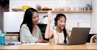 madre e bambino asiatico bambina che impara e guarda il computer portatile che fa i compiti studiando con il sistema di e-learning per l'istruzione online. videoconferenza per bambini con insegnante tutor a casa foto