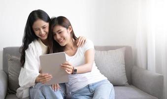 amante delle coppie lesbiche delle giovani belle donne asiatiche che utilizza la videochiamata del tablet online nel soggiorno sul divano di casa con la faccia sorridente concetto di sessualità lgbt con uno stile di vita felice insieme. foto