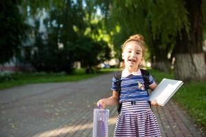 una bambina di aspetto caucasico in uniforme scolastica con uno zaino e il libro e un set di pennarelli. di nuovo a scuola. scuola elementare, sviluppando attività per bambini in età prescolare. spazio per il testo foto