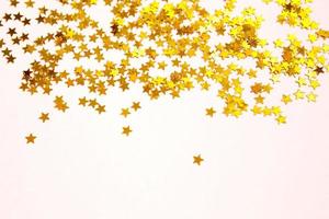 paillettes dorate a forma di stelle brillano su uno sfondo rosa. sfondi con copyspace per vacanze, decorazioni per feste, natale e capodanno, compleanno e anniversario. gradiente e consistenza foto