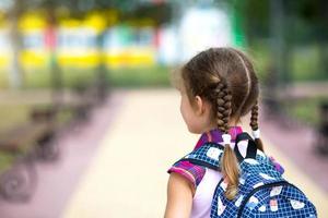 ragazza allegra con uno zaino e in uniforme scolastica nel cortile della scuola di nuovo al telaio. ritorno a scuola, 1 settembre. un allievo felice. istruzione primaria, classe elementare. strada per la vita, per la conoscenza foto