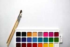 una tavolozza di acquerelli e pennelli a diciotto colori su sfondo bianco con spazio per il testo. foto