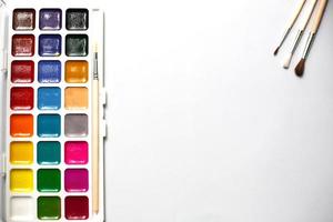 una tavolozza di acquerelli e pennelli a diciotto colori su sfondo bianco con spazio per il testo. foto