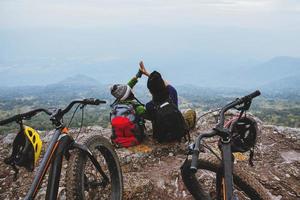 amante asiatico donna e uomo viaggiano natura. viaggiare relax andare in bicicletta deserto allo stato brado. sedersi su una scogliera rocciosa. foto