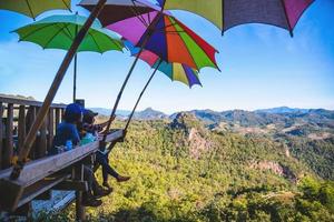 turisti asiatici coppia seduta mangiare noodle sulla piattaforma di legno e guardando la vista panoramica delle montagne della natura bellissima a ban jabo, mae hong son, thialand. foto