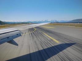 decollo dell'ala dell'aeroplano sulla pista con lo sfondo della montagna di neve foto
