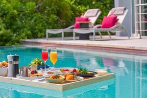 colazione in piscina, colazione galleggiante in resort tropicale. tavolo rilassante nell'acqua calma della piscina, colazione sana e piatto di frutta presso la piscina del resort. dieta estiva esotica. stile di vita da spiaggia tropicale foto