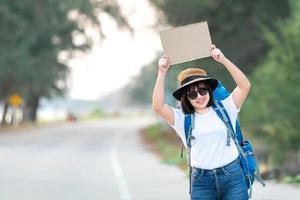 sorriso felice autostoppista donna asiatica zaino in attesa del trasporto in auto durante il fine settimana per il viaggio e il viaggio in vacanza all'ora del tramonto foto