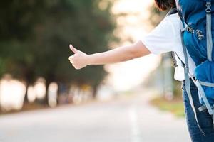 sorriso felice autostoppista donna asiatica zaino in attesa del trasporto in auto durante il fine settimana per il viaggio e il viaggio in vacanza all'ora del tramonto foto