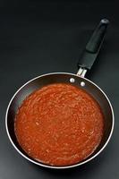 la salsa di pomodoro è preparata per cucinare come spaghetti o pasta in stile italiano in una padella nera su sfondo nero. vista dall'alto foto