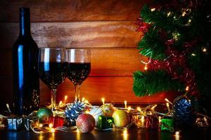 vino rosso in vetro trasparente, albero di Natale e ornamento su tavola di legno pronto per festeggiare. foto