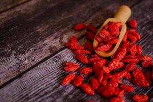 bacche di lupo cinesi essiccate o bacche di goji erbe cinesi o vite di matrimonio nella paletta di legno vicino a una ciotola di legno isolata su sfondo di legno. messa a fuoco selezionata. foto